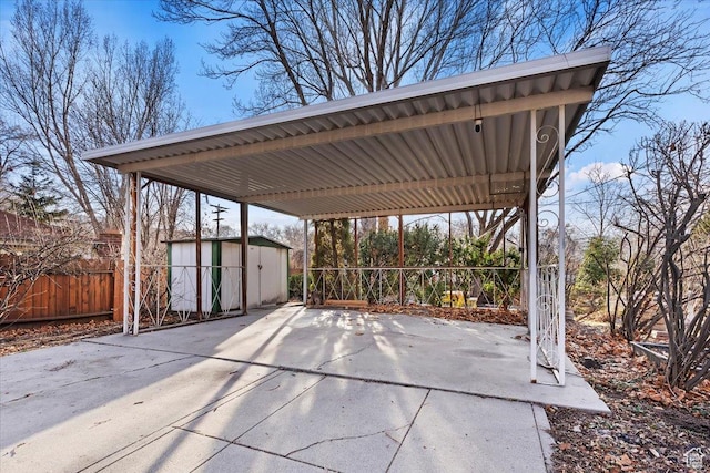 view of patio featuring a detached carport, concrete driveway, fence, a shed, and an outdoor structure