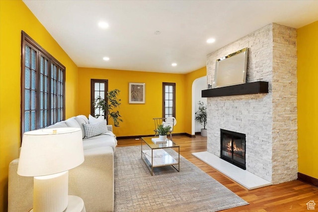 living room featuring a stone fireplace, recessed lighting, wood finished floors, and baseboards