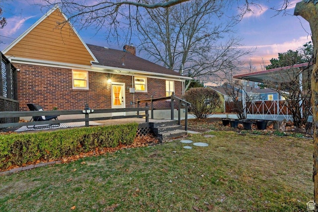 rear view of property with a wooden deck, a chimney, a lawn, and brick siding