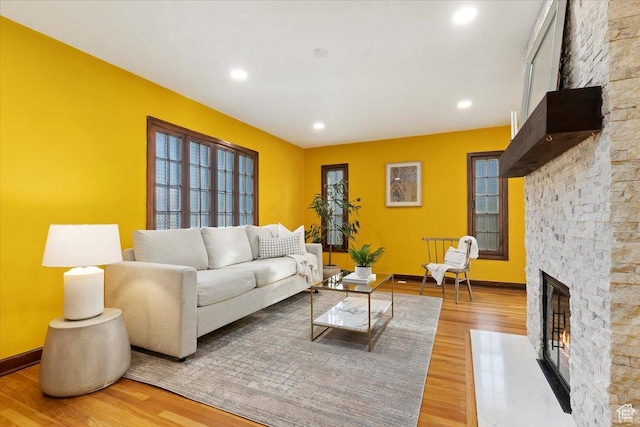 living area with light wood-style floors, recessed lighting, a stone fireplace, and baseboards
