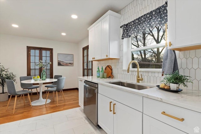 kitchen featuring light stone counters, white cabinets, a sink, and stainless steel dishwasher