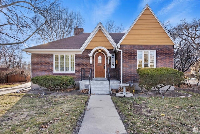 view of front facade with a front yard, a chimney, and brick siding
