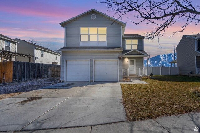 traditional-style house featuring an attached garage, a mountain view, fence, concrete driveway, and a front lawn