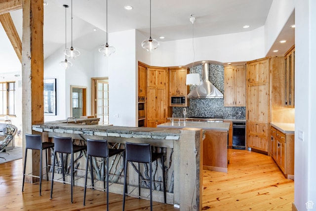 2667 Aspen Springs Dr, Park City, UT 84060 - kitchen with wall chimney exhaust hood, light wood-style floors, decorative backsplash, a breakfast bar, and recessed lighting