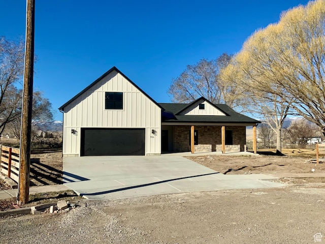 modern farmhouse featuring a garage, fence, concrete driveway, stone siding, and board and batten siding