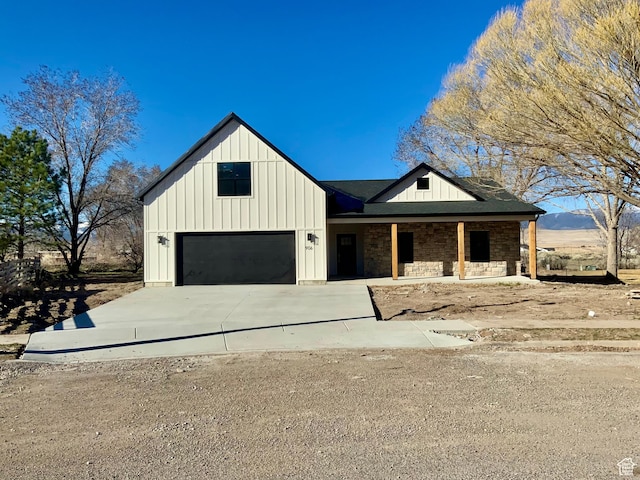 modern inspired farmhouse with a garage, stone siding, driveway, and board and batten siding