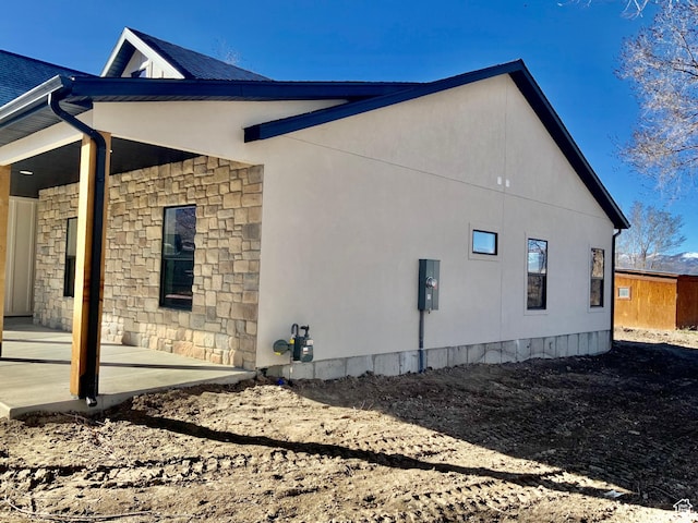 view of side of property featuring stone siding and a patio area