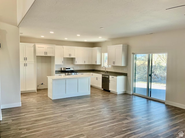 kitchen with appliances with stainless steel finishes, white cabinetry, a kitchen island, wood finished floors, and baseboards