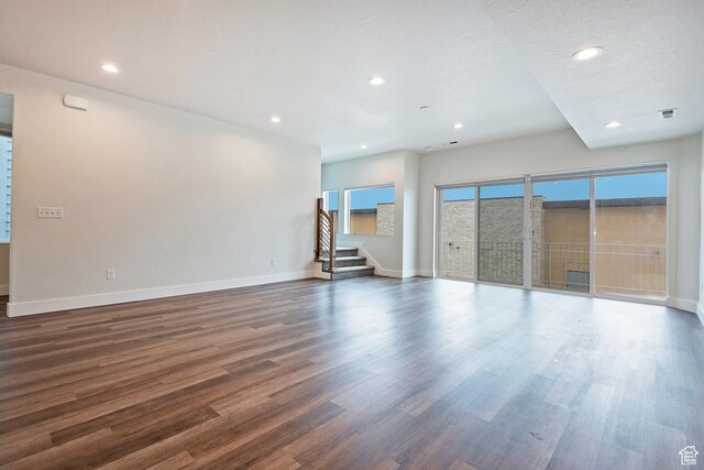 unfurnished living room with recessed lighting, stairway, dark wood-type flooring, a textured ceiling, and baseboards