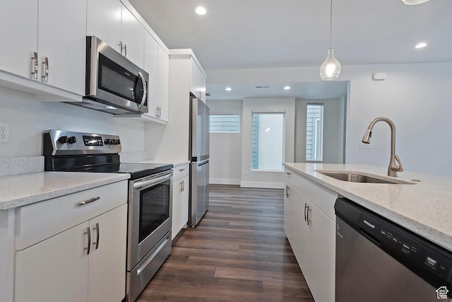 kitchen featuring white cabinets, appliances with stainless steel finishes, light stone countertops, pendant lighting, and a sink