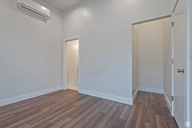 empty room featuring dark wood-style flooring, a wall unit AC, and baseboards