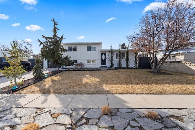 split level home with driveway, board and batten siding, a front yard, and fence