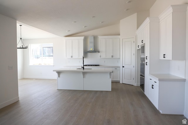 2794 E Liam Ln Unit 101, Eagle Mountain, UT 84005 - kitchen with wall chimney range hood, vaulted ceiling, white cabinetry, tasteful backsplash, and a center island with sink