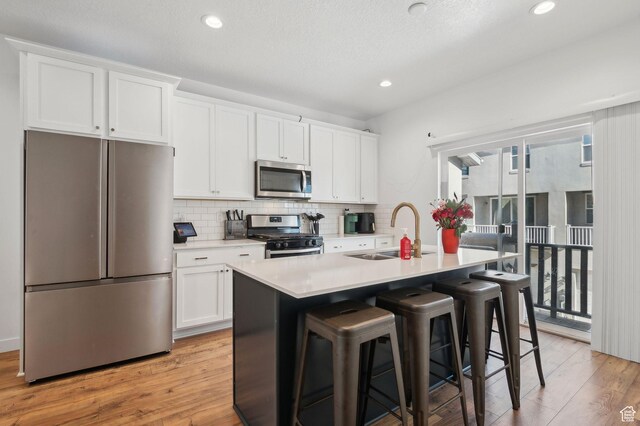 6643 W Skip Rock Rd S, South Jordan, UT 84009 - kitchen with a kitchen island with sink, stainless steel appliances, a sink, white cabinets, and light countertops