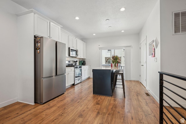 6643 W Skip Rock Rd S, South Jordan, UT 84009 - kitchen featuring visible vents, white cabinets, appliances with stainless steel finishes, a breakfast bar, and a kitchen island with sink