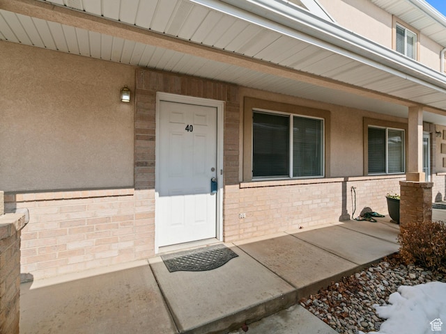 entrance to property featuring stucco siding, a porch, and brick siding
