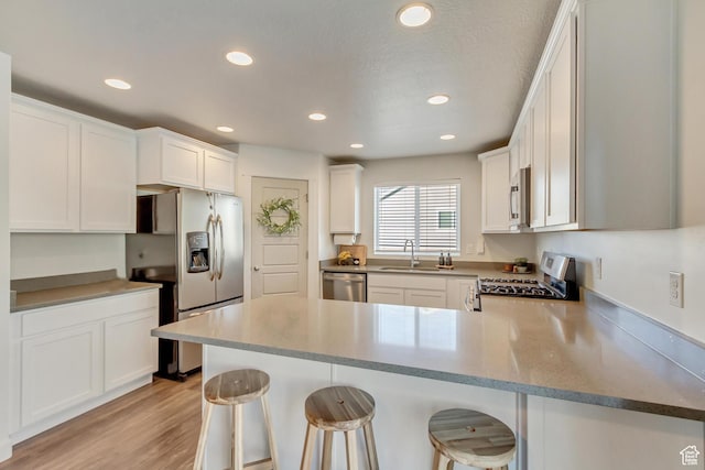 6393 N Pine Tree Way, Eagle Mountain, UT 84005 - kitchen featuring a sink, white cabinetry, a peninsula, stainless steel appliances, and light wood-style floors
