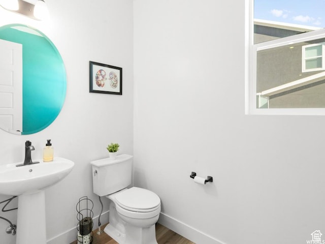 half bath featuring a sink, wood finished floors, toilet, and baseboards