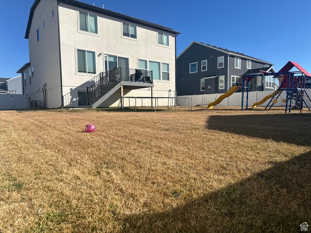back of house with central AC unit, playground community, fence, a yard, and stucco siding