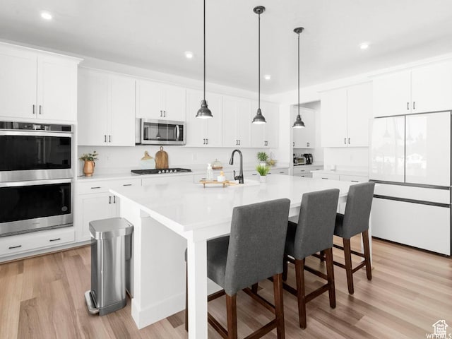 kitchen with an island with sink, decorative light fixtures, stainless steel appliances, light countertops, and white cabinetry