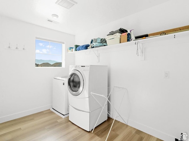clothes washing area featuring laundry area, baseboards, wood finished floors, and washing machine and clothes dryer