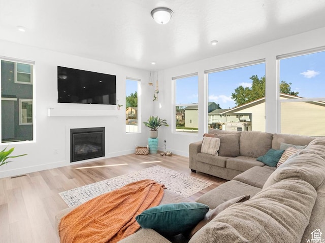 living room featuring light wood-type flooring, baseboards, and a glass covered fireplace