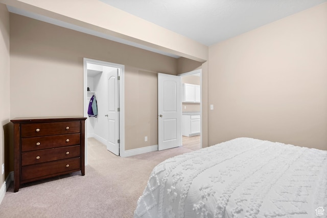 bedroom featuring light carpet, a spacious closet, and baseboards
