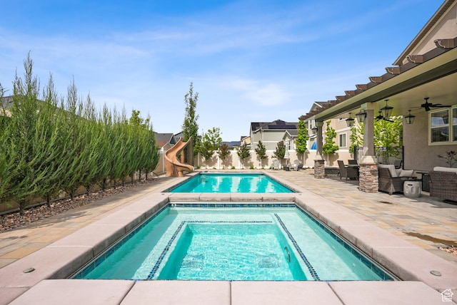 view of swimming pool with a water slide, a fenced backyard, a ceiling fan, a patio area, and an in-ground hot tub