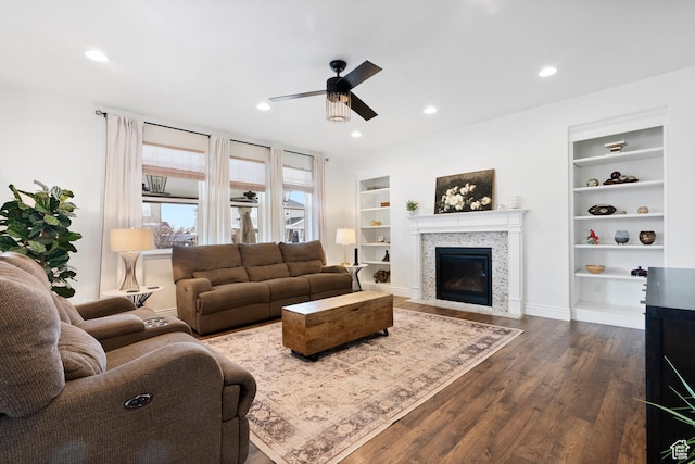 living room with a ceiling fan, recessed lighting, built in features, a fireplace with flush hearth, and dark wood-style floors