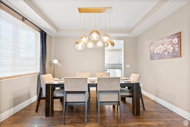 dining space with a tray ceiling, a chandelier, baseboards, and wood finished floors