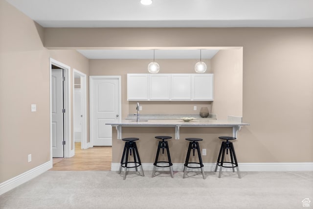 kitchen with hanging light fixtures, a breakfast bar, white cabinets, light stone countertops, and light carpet