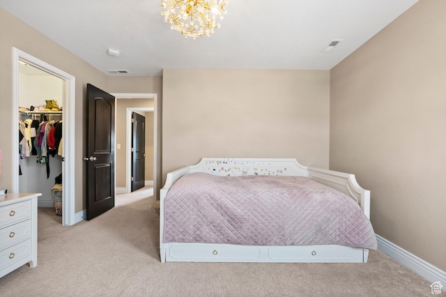 bedroom with light carpet, a walk in closet, a chandelier, and baseboards