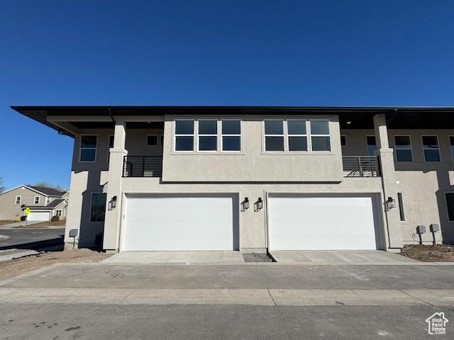 multi unit property featuring a garage, a balcony, and stucco siding
