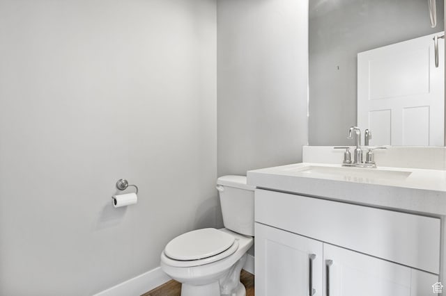 half bathroom with toilet, vanity, baseboards, and wood finished floors