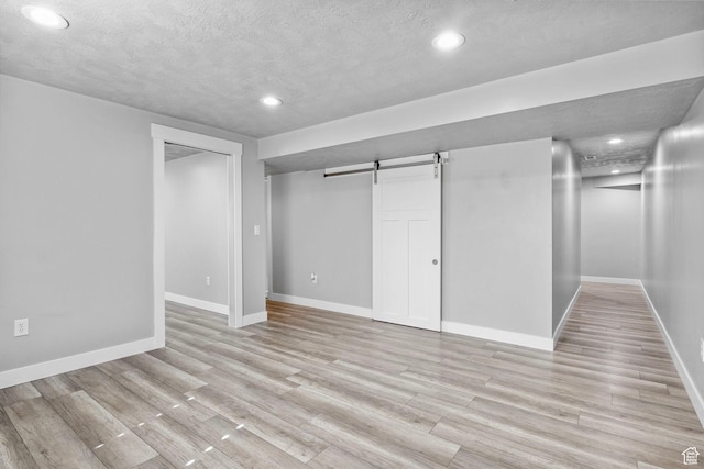 basement with recessed lighting, baseboards, light wood-style floors, and a barn door