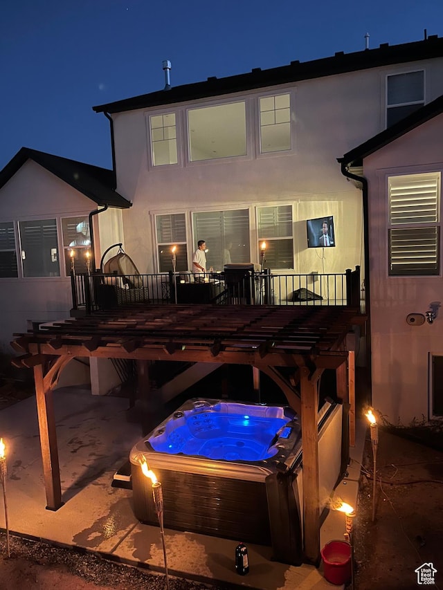 back of house at night with stucco siding, a wooden deck, and an outdoor hot tub