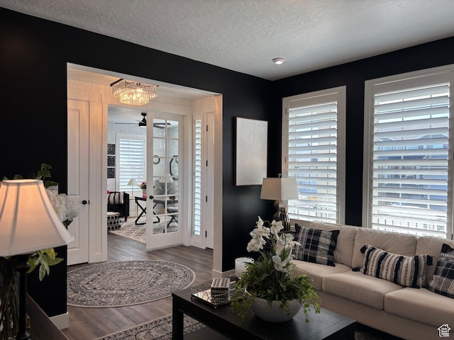living area featuring an inviting chandelier, wood finished floors, a textured ceiling, and a healthy amount of sunlight