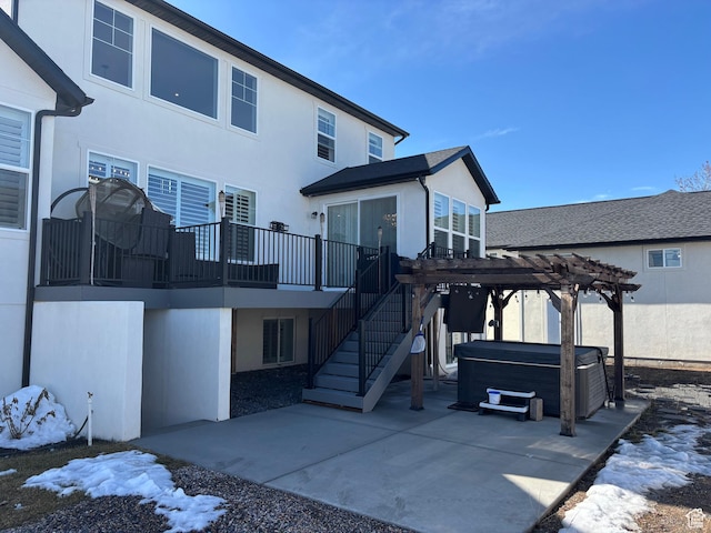 rear view of house with stucco siding, a pergola, a hot tub, and a patio area