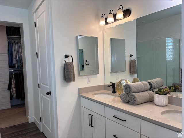 bathroom with a walk in closet, double vanity, wood finished floors, and a sink