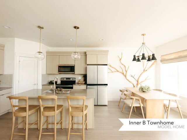 kitchen featuring a kitchen island with sink, decorative backsplash, appliances with stainless steel finishes, a kitchen bar, and light wood-type flooring