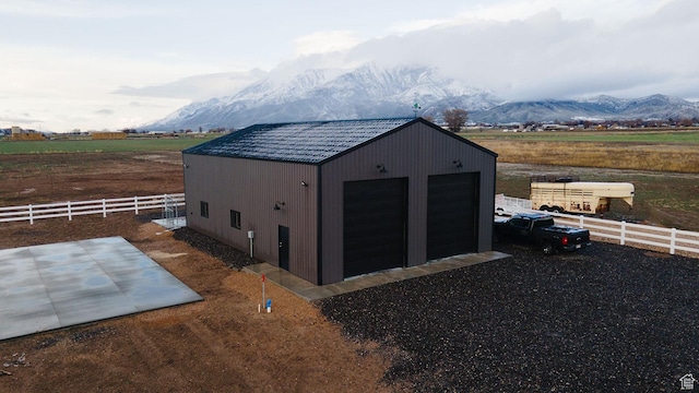 view of outdoor structure with a rural view, fence, a mountain view, and an outbuilding