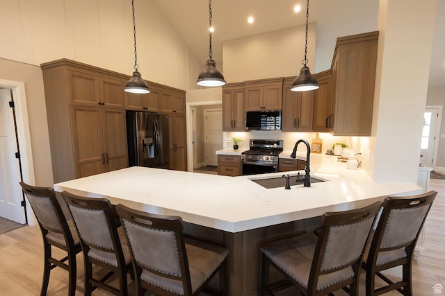 kitchen featuring a peninsula, stainless steel gas range, black refrigerator with ice dispenser, high vaulted ceiling, and a sink