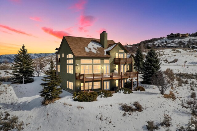 snow covered house with a balcony, a chimney, and stucco siding