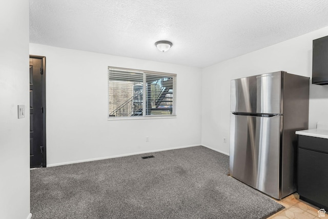 interior space featuring visible vents, light colored carpet, a textured ceiling, and freestanding refrigerator