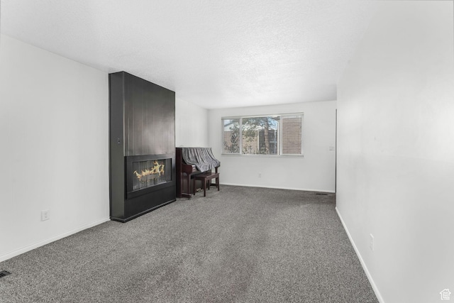 unfurnished room with carpet floors, a glass covered fireplace, a textured ceiling, and baseboards