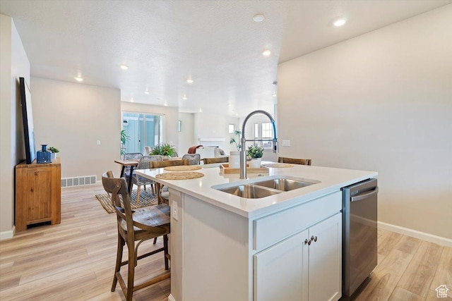 kitchen featuring light wood finished floors, visible vents, dishwasher, open floor plan, and a sink