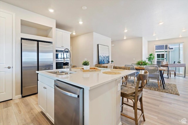 kitchen with a center island with sink, white cabinets, light wood-style flooring, stainless steel appliances, and a sink
