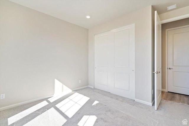 unfurnished bedroom featuring a closet, light colored carpet, visible vents, and baseboards