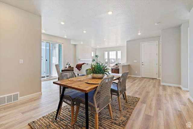 dining space featuring light wood-type flooring, baseboards, visible vents, and a textured ceiling