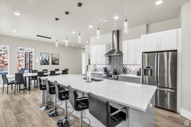 5159 W 2200 S, Hurricane, UT 84737 - kitchen featuring light wood-style flooring, visible vents, appliances with stainless steel finishes, decorative backsplash, and wall chimney exhaust hood
